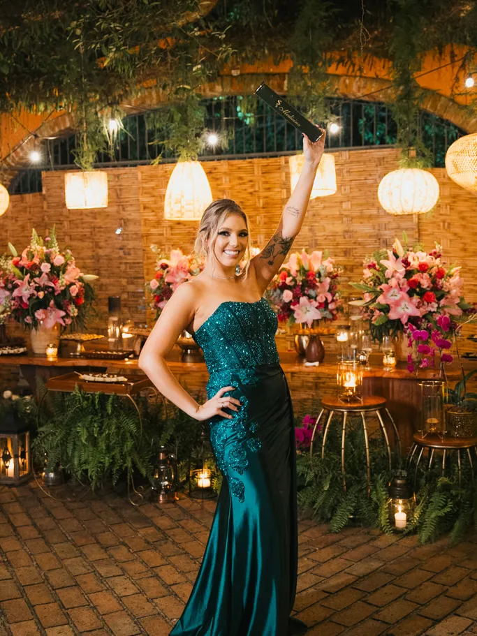 Formanda de vestido verde comemorando no jardim decorado com lanternas