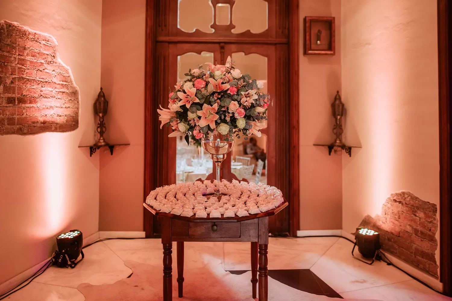 Mesa de doces com arranjo de flores rosadas diante da porta de madeira